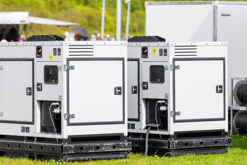 Set two large portable industrial power fuel generator green lawn at commercial event outdoors clear blue sky background. Mobile electricity supply energy plant unit backup equipment rent service.